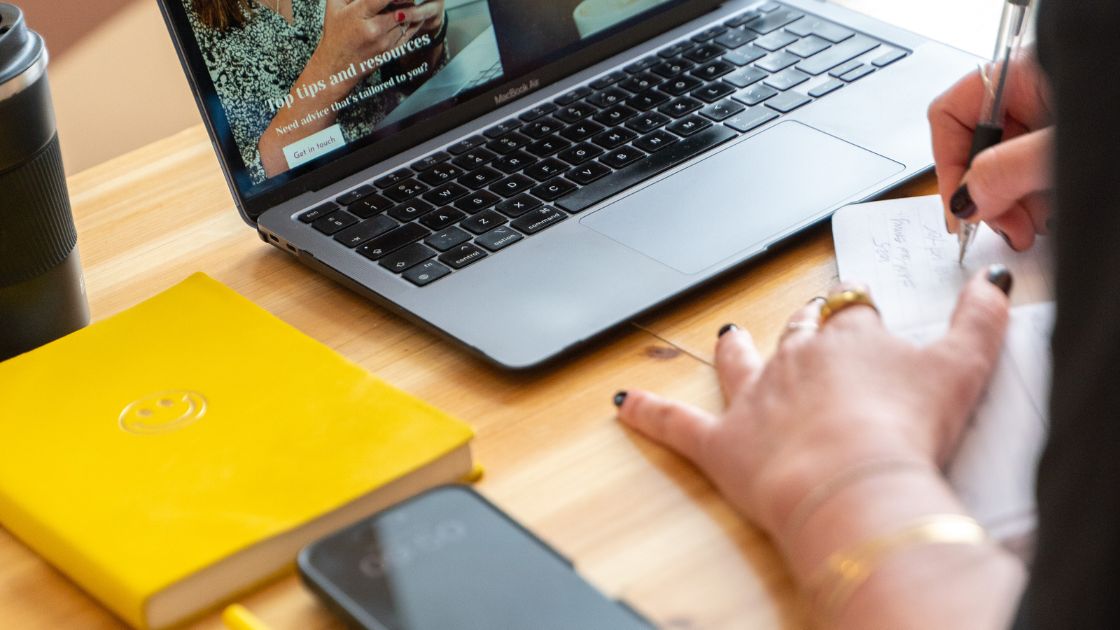 A MacBook, yellow notebook and an iPhone on a desk