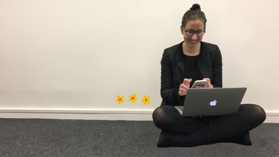 A woman in business sitting on the floor of an empty office with a MacBook and phone on her lap