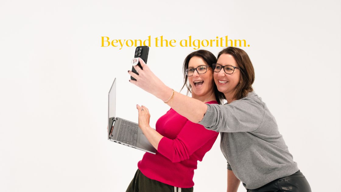 two women in business owners, standing together and one is holing a laptop and phone
